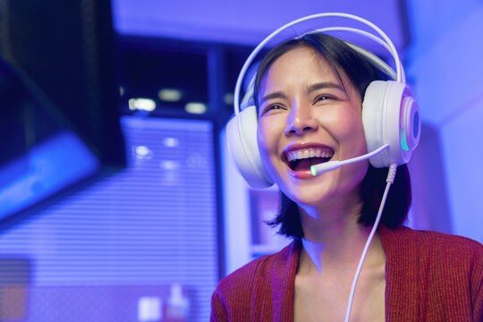 Excited young Asian girl playing online computer game with headset and microphone at home, esports and live streaming concept.