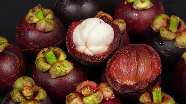 A cinematic macro loop of an open purple mangosteen fruit rotating among wet tropical produce.