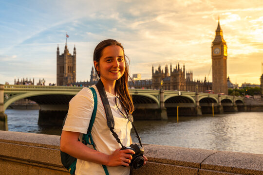 Female tourist photographer with camera near Palace of Westminster, Big Ben clock tower and Westminster Bridge at sunset in London, England, UK