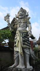 Obraz premium Giant statues, also known as bhuta kala, Dwarapala, gatekeeper statues carrying cups, torches, and weapons, with frightening faces. They wear Balinese poleng cloth. Photo raw, no edit.