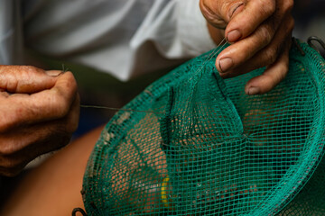 Detailed shot of senior hands pulling a nylon string to fix a green mesh fishing trap cage © Nguyen Tuan