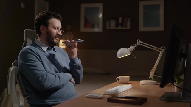 Voice message, freelancer at work concept. Male freelancer in home office uses phone to record voice message