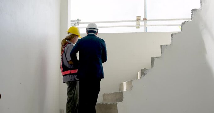 Two construction professional walk through unfinished stairwell, inspector and worker review concrete structure progress while checking workplace safety inside building project site area indoors