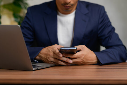 Man in Suit Using Mobile Phone While Sitting at Desk with Laptop
