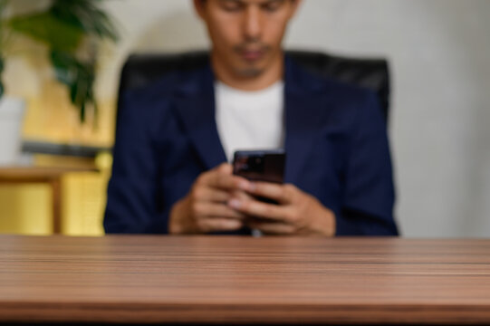 Young Man Using Smartphone While Sitting at Wooden Desk