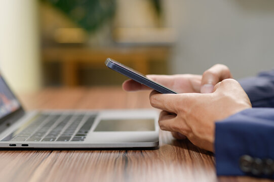 Hands Using Smartphone While Working on Laptop at Wooden Table