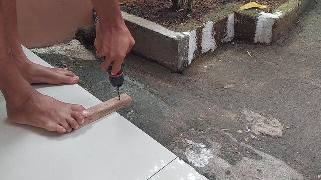 Drilling holes in a wooden board with a cordless drill at home during a work holiday, enjoying a DIY woodworking and home improvement project.