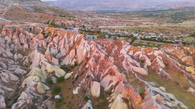 Goreme, Nevsehir, Turkey. Red Valley viewpoint at golden hour, aerial drone footage over eroded tuff formations and crowded observation area with parked buses and cars. Aerial View