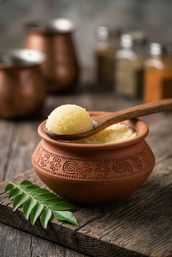 Spoonful of desi ghee in a clay pot with curry leaves on a wooden table