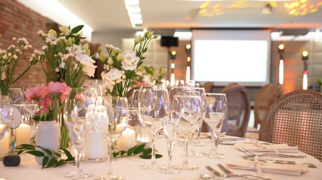 Wide angle shot of a beautifully decorated banquet hall table, featuring fresh flowers, glowing candles, sparkling glassware, and soft, warm lighting in a chic, modern event setting.