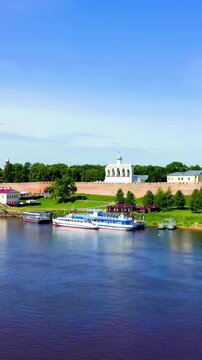 Vertical video. Veliky Novgorod, Russia. The Novgorod Kremlin (Detinets), a UNESCO-listed red-brick fortress with swallowtail merlons, rising above the Volkhov River under a clear summer sky.. Drone 