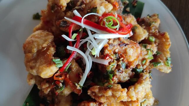 Close-up video of crispy fried seafood topped with sliced chili, spring onions, and savory seasoning. Delicious Asian-style dish with crunchy texture and vibrant garnish, perfect for restaurant, culin