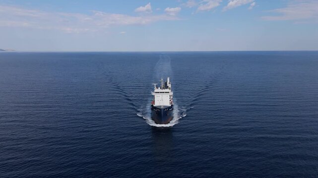 Aerial tracking shot of a large industrial cargo ship moving across calm ocean waters. Concept of global maritime logistics and transportation.