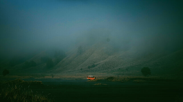 An orange 4x4 vehicle in the middle of a heavy fog in the volcanic caldera of Mount Bromo