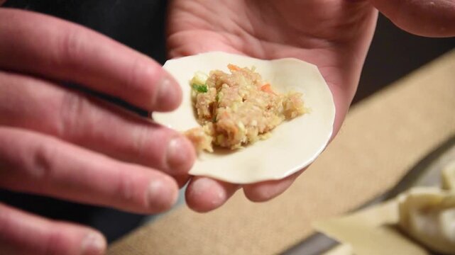 Close-up view of a chef's hands skillfully folding and crimping a raw gyoza dumpling filled with minced pork and vegetables