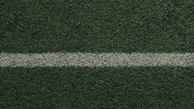 Soccer ball rolling across green artificial turf field with lines