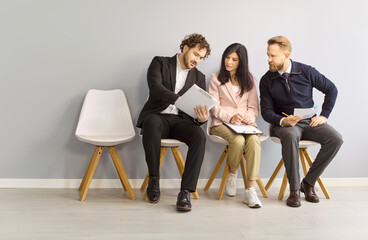 Obraz premium Candidates in interview recruitment hiring waiting discussion. Applicants review a resume on a tablet before meeting in bright modern office. Teamwork and preparation before formal hiring.