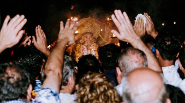 Crowded group of devotees with raised hands worshiping a glowing deity statue during a traditional festival for religious news, cultural editorial and travel promotion