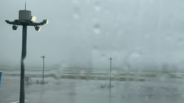 Empty airport tarmac and floodlight tower seen through wet window with trickling water during severe typhoon with heavy rain audio