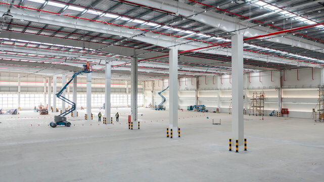 Vast Industrial Warehouse Construction: An expansive, unfinished warehouse interior showcases industrial construction with high ceilings, exposed beams, and a scissor lift.
