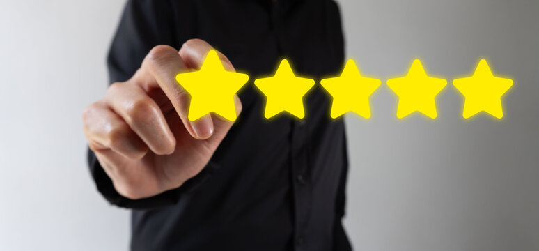 Hand taps five glowing stars, symbolizing high satisfaction. Dark shirt contrasts with bright, vibrant yellow stars. Finger gestures toward rating, implying approval or excellence