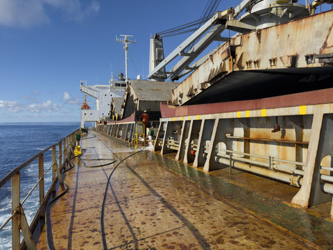 ship main deck and hatch covers partly opened. cranes, crew working. daily works of seafarers. 
