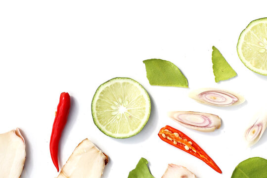 A colorful, close-up pattern of Thai herbs: lime slices, galangal, lemongrass, chilies, and kaffir lime leaves.
