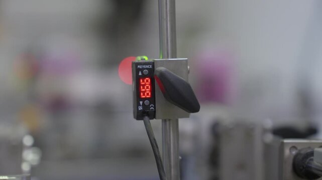 Keyence digital sensor with red LED readout mounted on steel rail on active production line