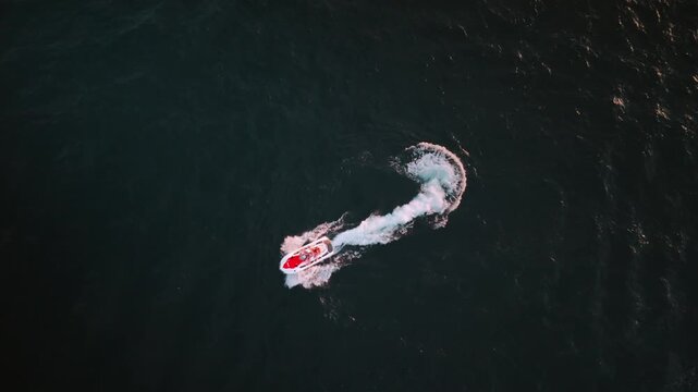 Vertical drone shot of speedboat making sharp turn on dark ocean water
