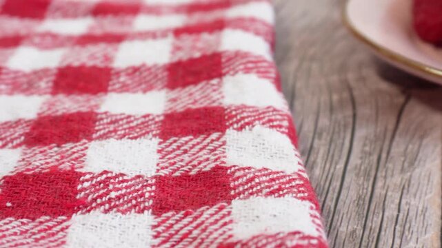 A panning shot from a checkered tablecloth to fresh raspberries resting on a small plate. The raspberries look juicy and ripe, with a blurred background.