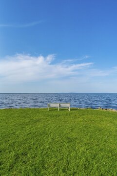 Isolated, white, empty bench in a meadow on the shore of the Szczecin Lagoon in the village of Altwarp, Am Stettiner Haff nature park Park, Mecklenburg-Western Pomerania, Germany