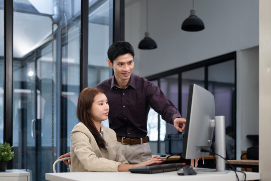 Two Asian from two different generations work and share information via desktop computer at their desks in a modern office, ideal for teamwork and collaboration in the workplace