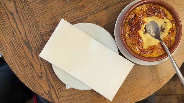 POV Point of vioman's hands gently putting down a cup of hot cappuccino on a wooden table in a traditional french cafe in Paris, next to a delicious cr&egrave;me br&ucirc;l&eacute;e ready to be eaten for a relaxing break