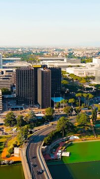 Vertical video. Rome, Italy. Panoramic Drone footage over the EUR district, a modernist complex of travertine and concrete buildings arranged on axial grids, with a curved highway and an artificial l