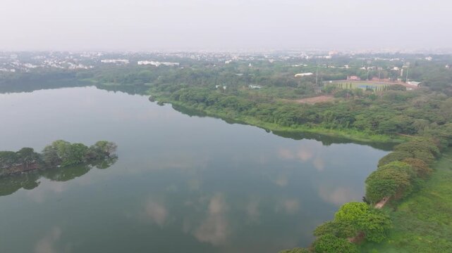 Kukkarahalli Lake with Srikantadatta Narasimha Raja Wadeyar Cricket Stadium, haze and greenery at Mysuru, karnataka, india. day time, push back shot, drone shot, 4k.