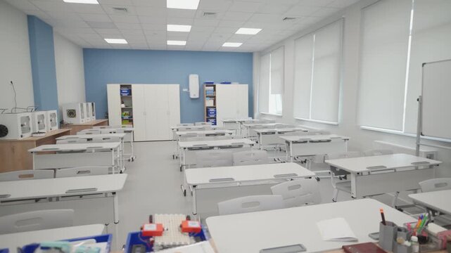 Robotics kits inside blue trays sit on foreground table in classroom. Minimalist engineering laboratory looks organized and fresh