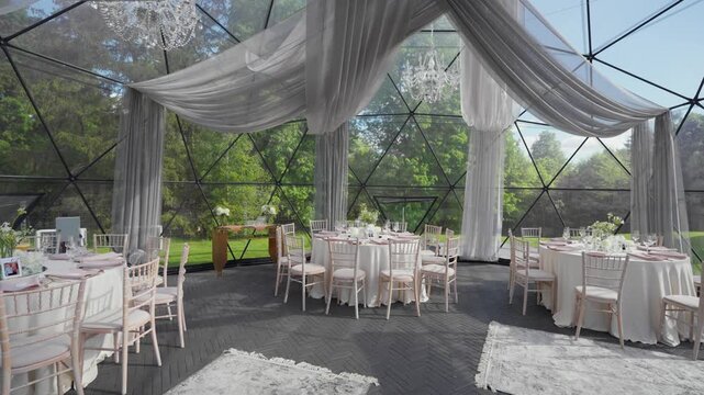 Spacious geodesic dome wedding venue with natural light, draped fabric, crystal chandeliers, and round tables elegantly set. Serene garden view and soft daylight add sophistication. (198 characters)