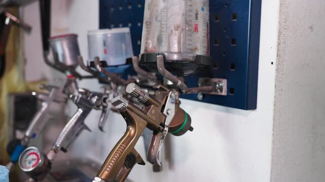 Professional HVLP spray guns hanging on a workshop wall in an automotive paint shop with shallow depth of field, showcasing industrial tools and vehicle refinishing equipment in UHD.