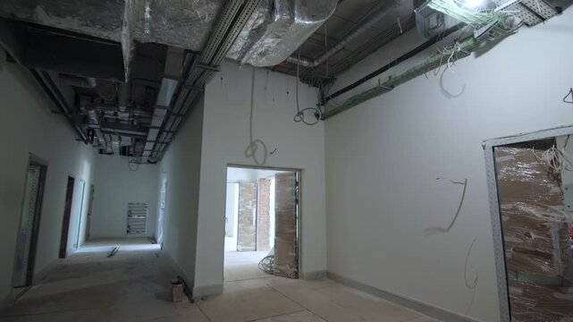 Industrial ventilation systems hang above messy plywood floor panels. Open doorways reveal raw brick wall sections inside building site