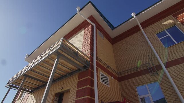 Unfinished metal porch structure attaches to modern institutional facade. Clear daytime weather highlights active construction process