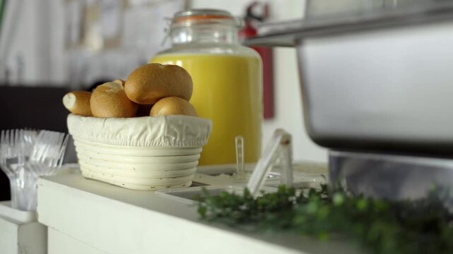 Fresh bread rolls arranged in basket beside juice container on catering service counter with breakfast setup and dining atmosphere indoors