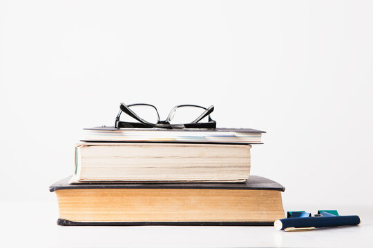 stack of books with eyeglasses and pen on a white background