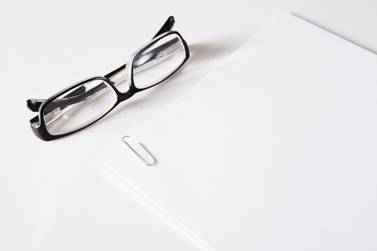 Black eyeglasses and white paper on a white background with copy space
