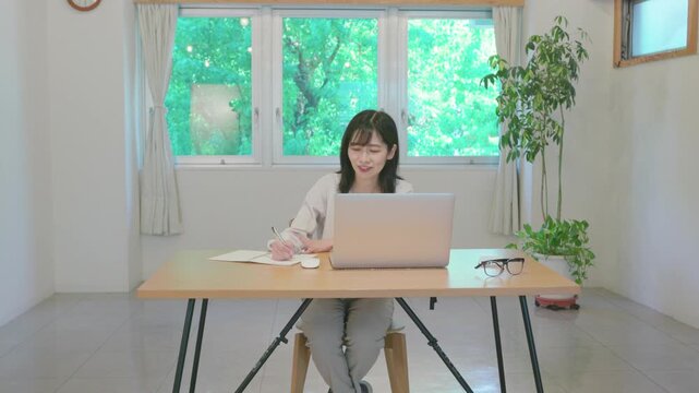 Young asian woman taking notes in notebook while working on laptop