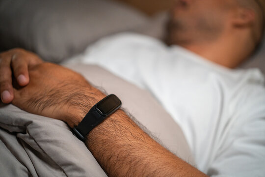 Use a smartwatch to track sleep and check for quality sleep. Young man lying in the bed at night. Man sleeping well in comfortable cozy fresh bed on soft pillow linen. Health and rest concept.