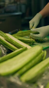 Close-up of female hands peeling bitter melon at Asian market. Delicious exotic vegetables sold at street markets.