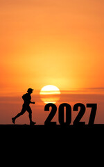 Fototapeta premium Silhouette of a man running towards the sunrise with the year 2027 depicted in large numerals. This image symbolizes the pursuit of goals, new beginnings, and the passage of time in the upcoming year.
