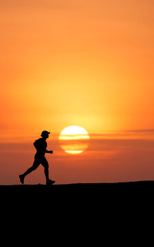 Silhouette of a man running at sunset, with the sun low on the horizon, casting a warm orange glow across the sky. The runner appears determined as they move forward.