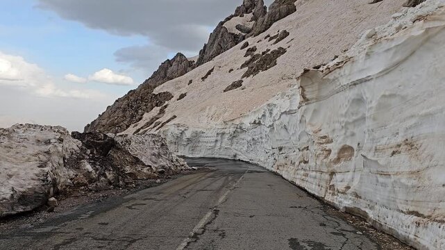 Spring mountain road carved between tall snow walls in Tette heights, showing melting layers and rugged slopes under a dramatic cloudy sky.
📍Tatte, Hawraman Takht, Kurdistan 