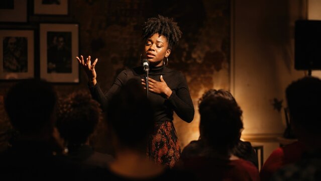 Emotive spoken-word poet performing on a small intimate stage under warm spotlight